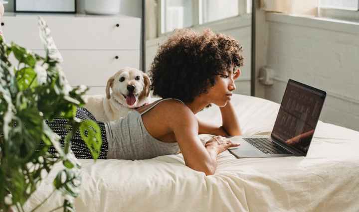 relaxed black woman watching laptop near dog on bed